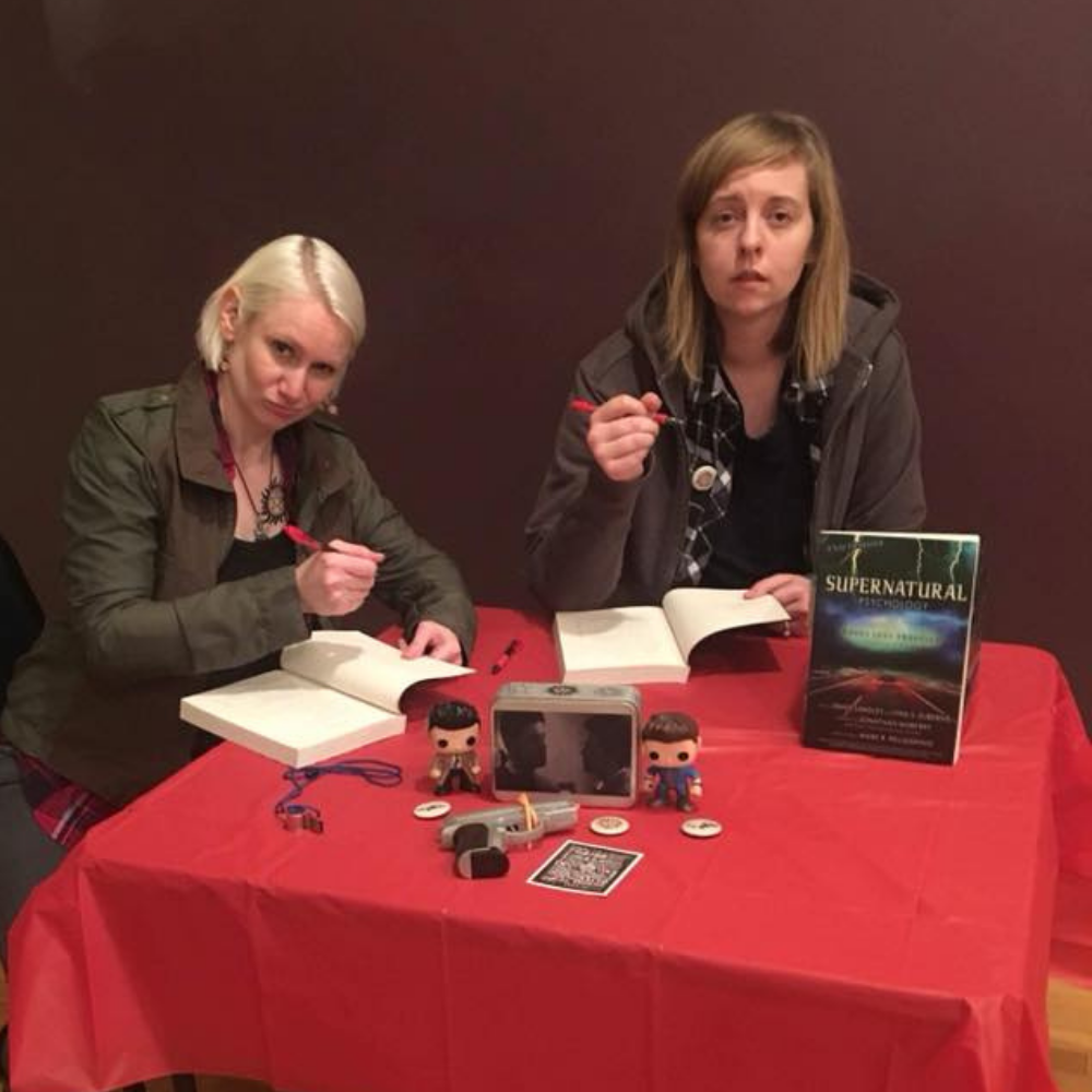 Justine and Larisa dressed as characters from Supernatural as they sign copies of their book.